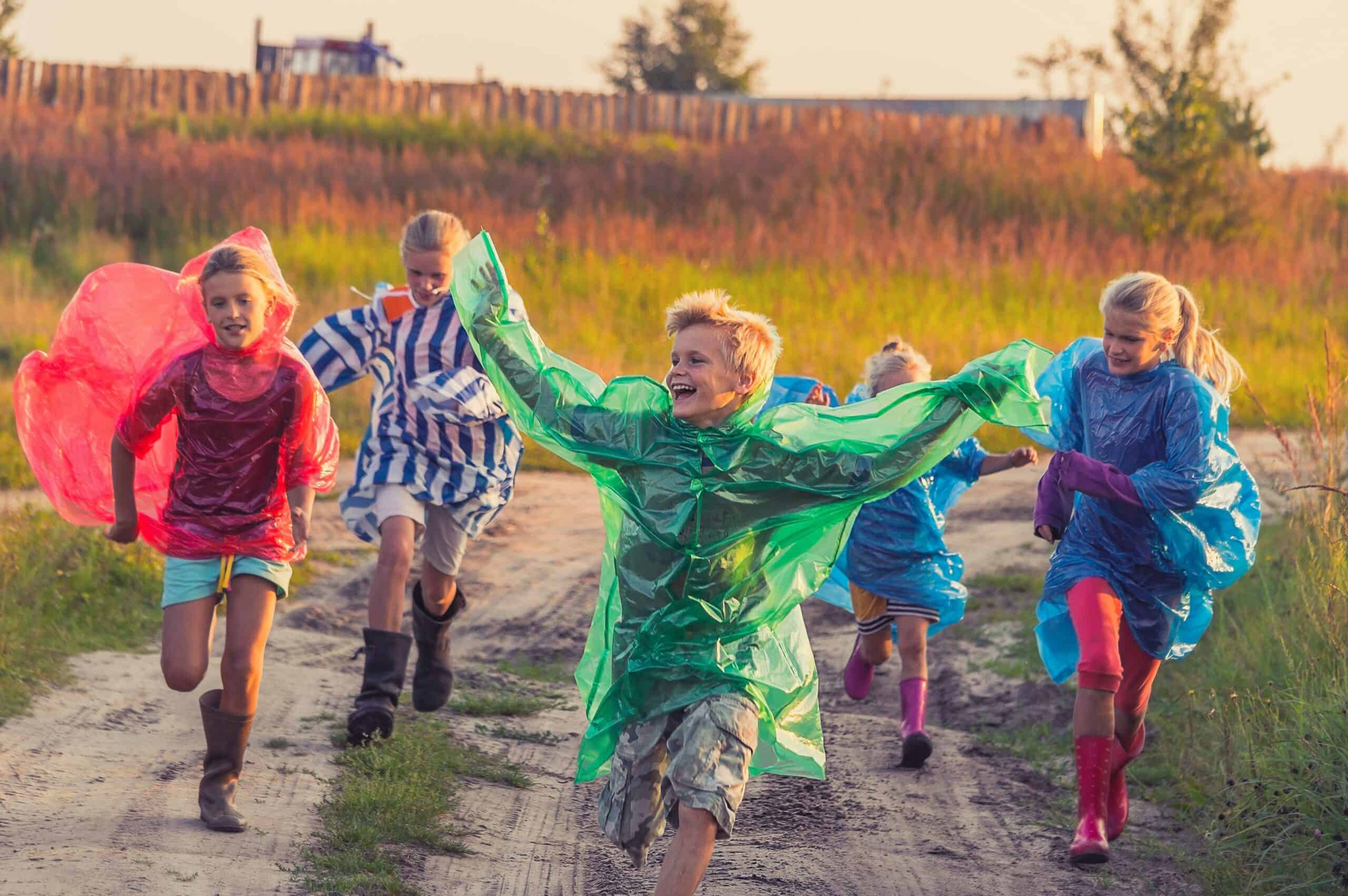 Children running down a farm track smiling in multicoloured rain ponchos