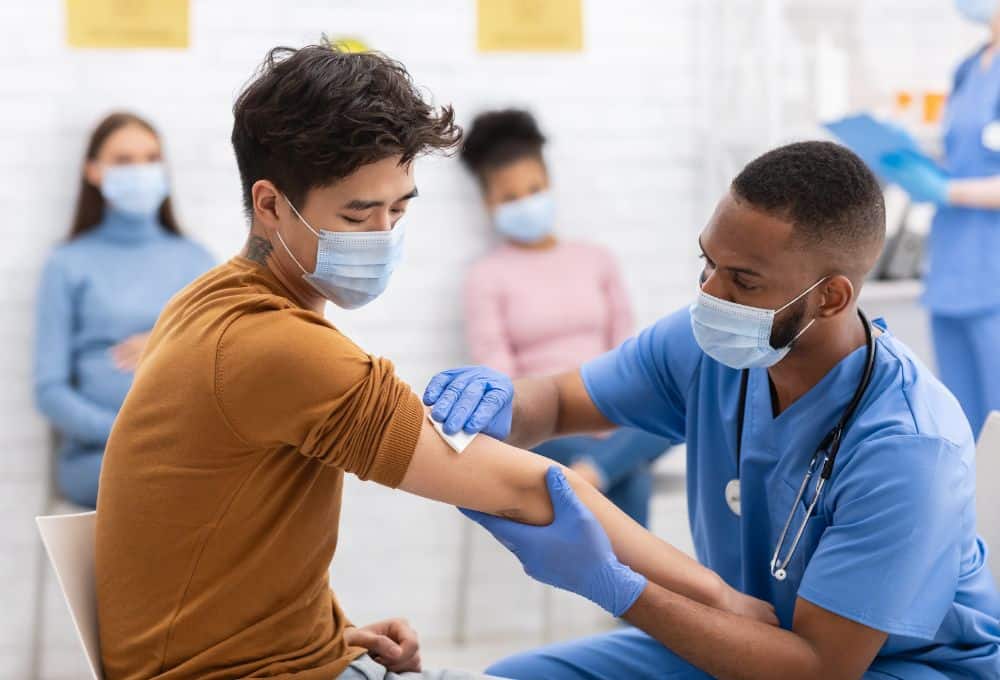 A clinician preparing to vaccinate someone in their arm, with other people waiting in the background