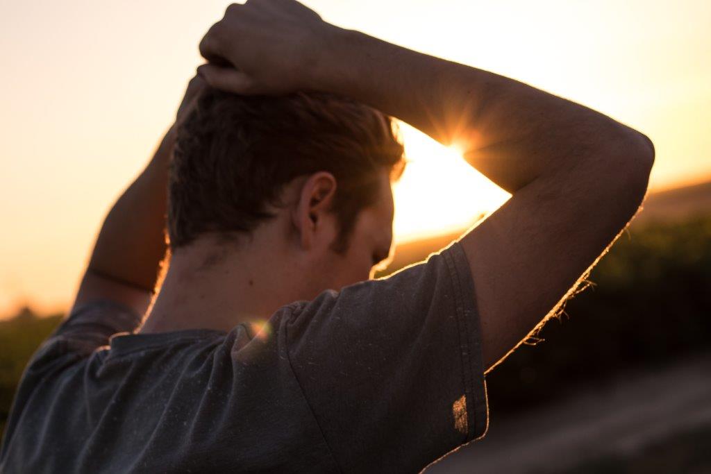 Decorative image of a person facing the sunset with their hands on their head.