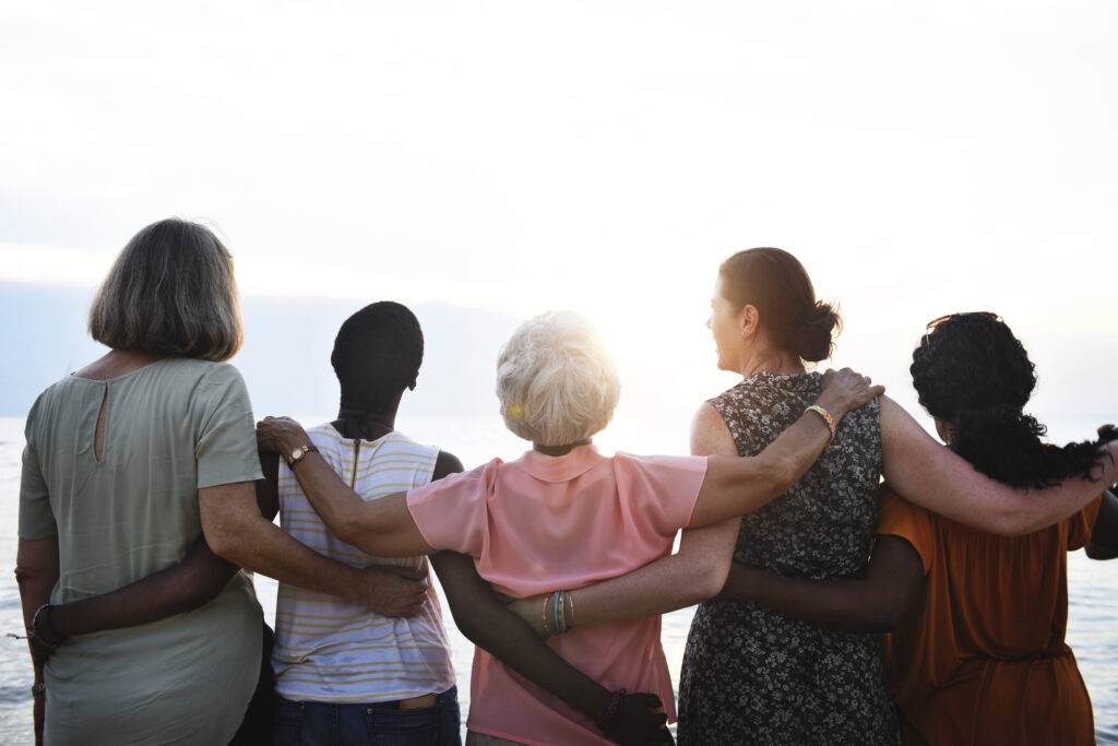 Group of people with their arms around each others shoulders looking into the sunset.