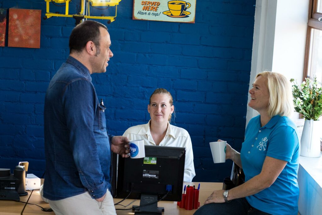 Three people having a conversation around an office desk and computer