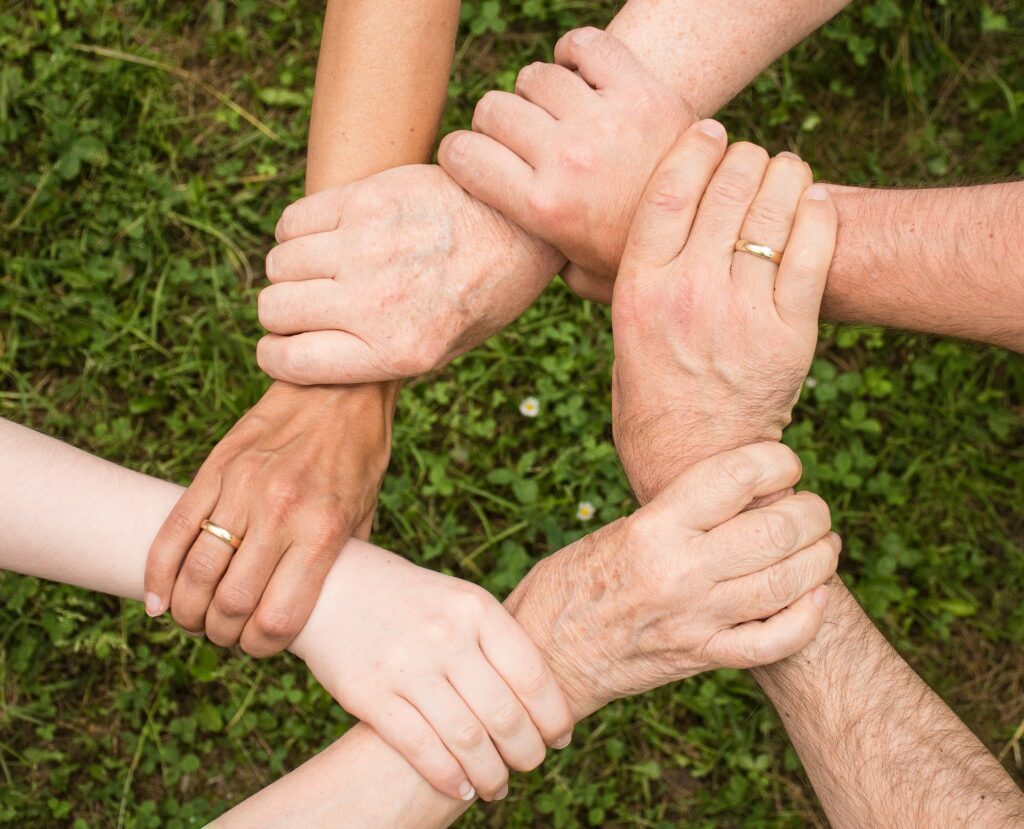 A picture of six interlocking hands holding the wrist of another person