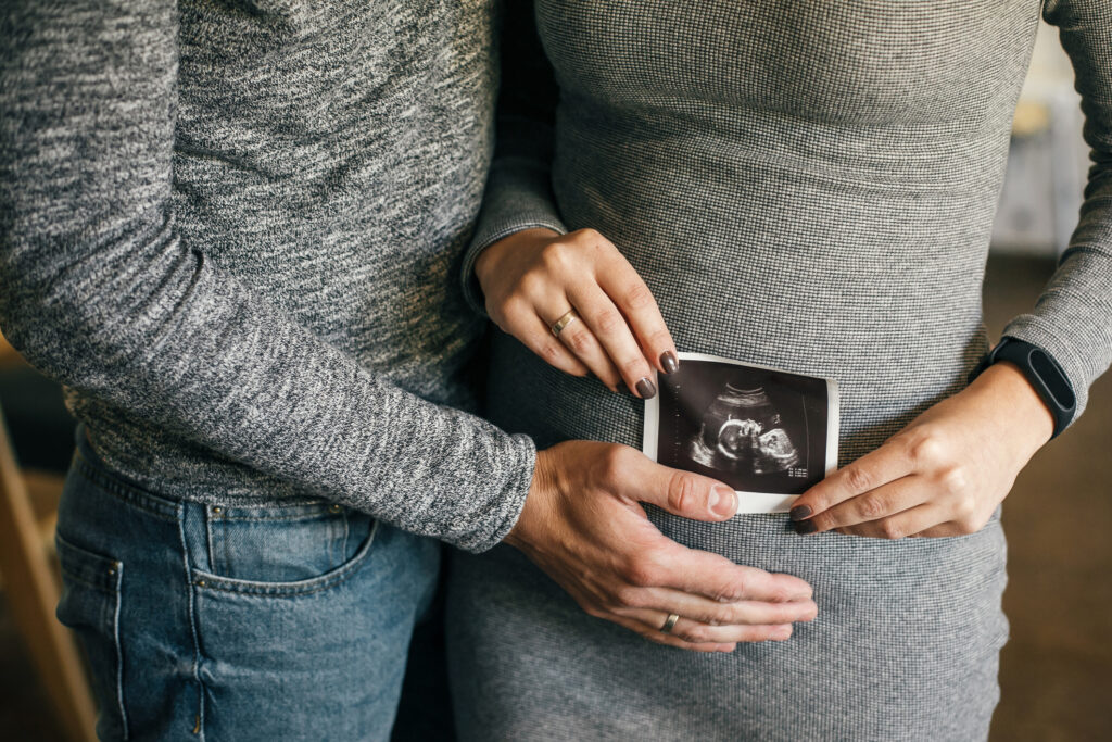 Two people with a baby scan and one hand on pregnant belly