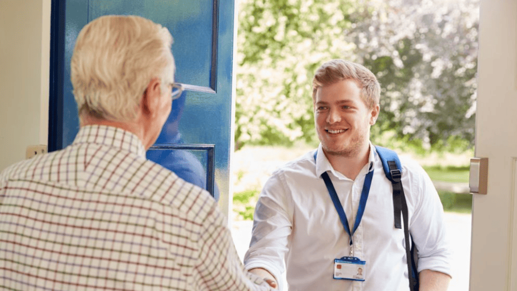Image of a white male with a bag and official lanyard smiling and shaking hands with an older white male wearing glasses who has just opened the door.