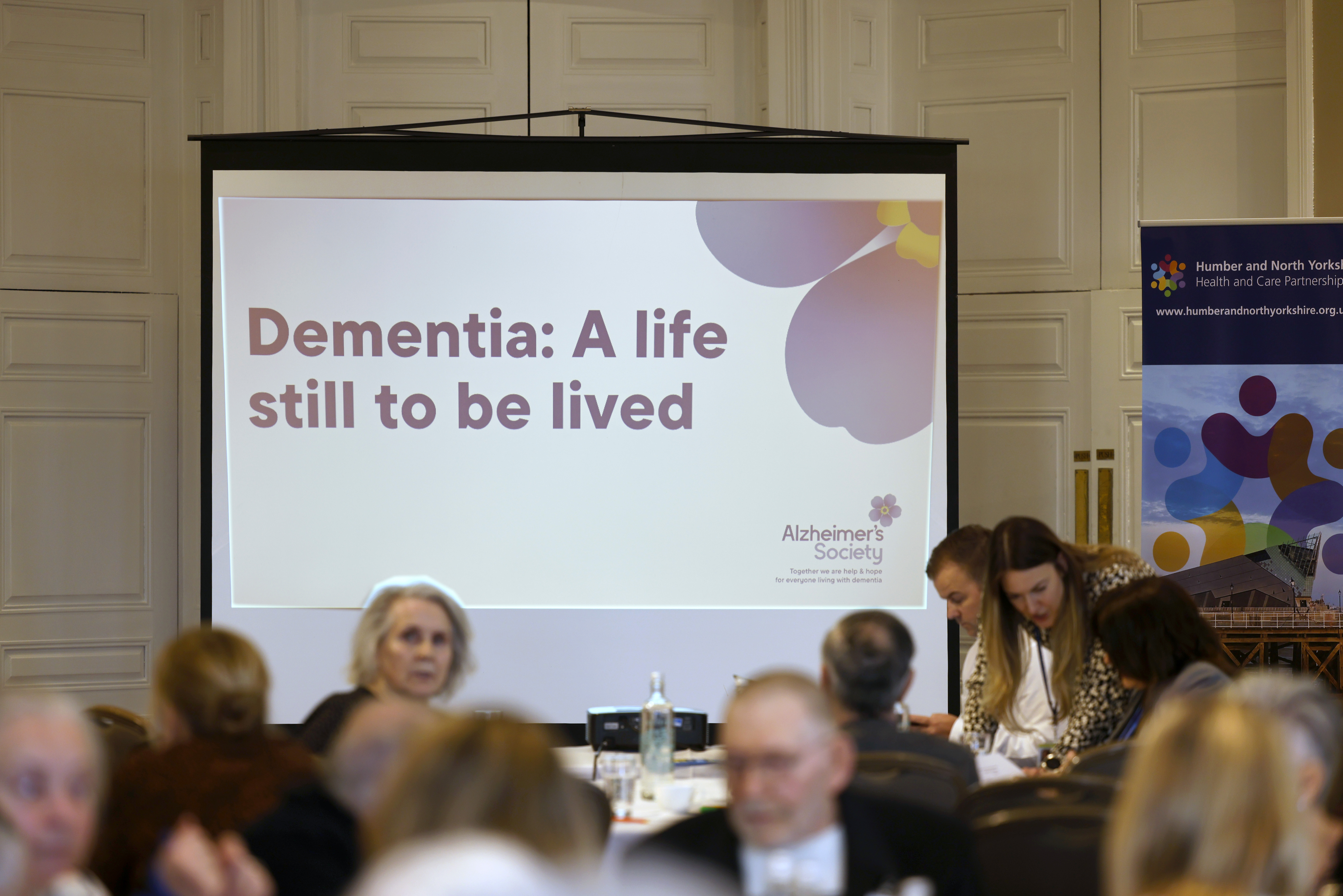 Picture of people at the conference with the presentation slide titled 'Dementia: A life still to be lived' in the background