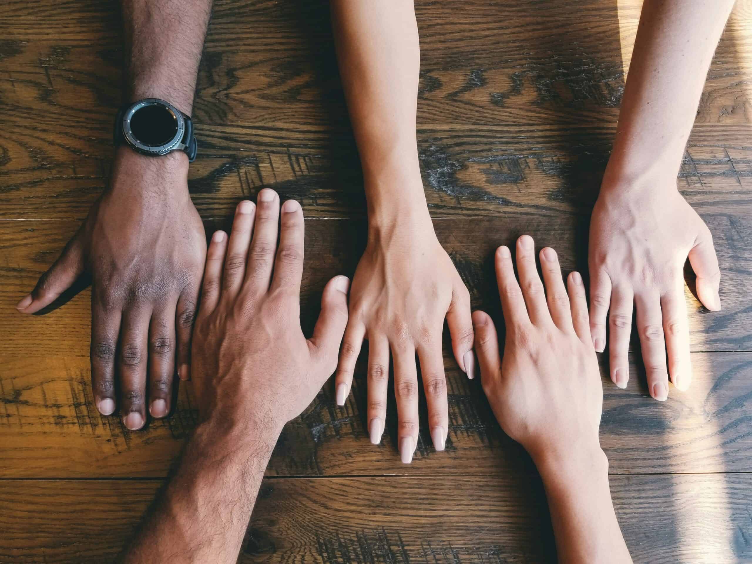 Five hands on a table of different ethnic backgrounds to depict diversity in out communities