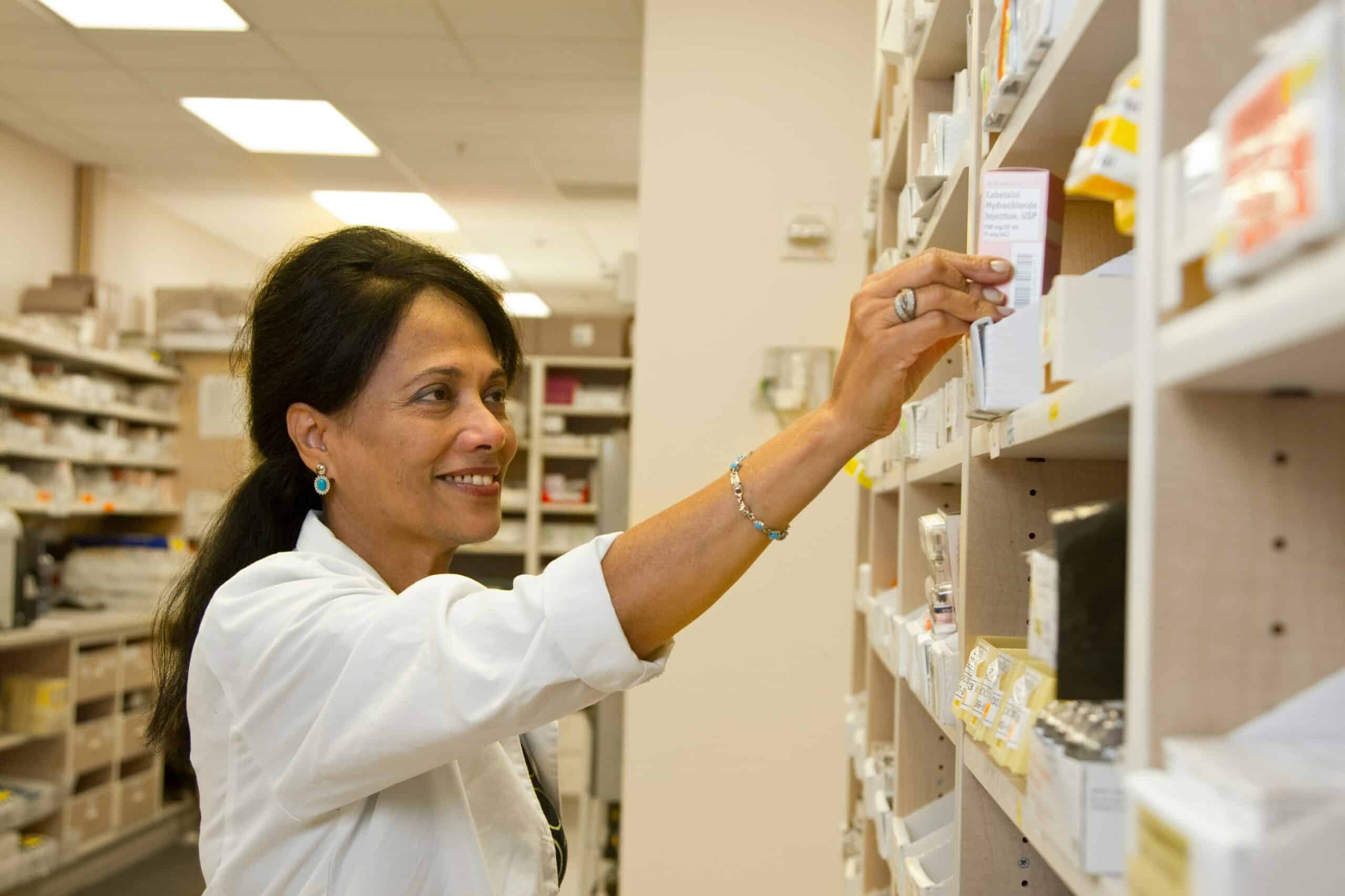 Pharmacist in a chemist reaching to a shelf with medicines on. Chemist setting